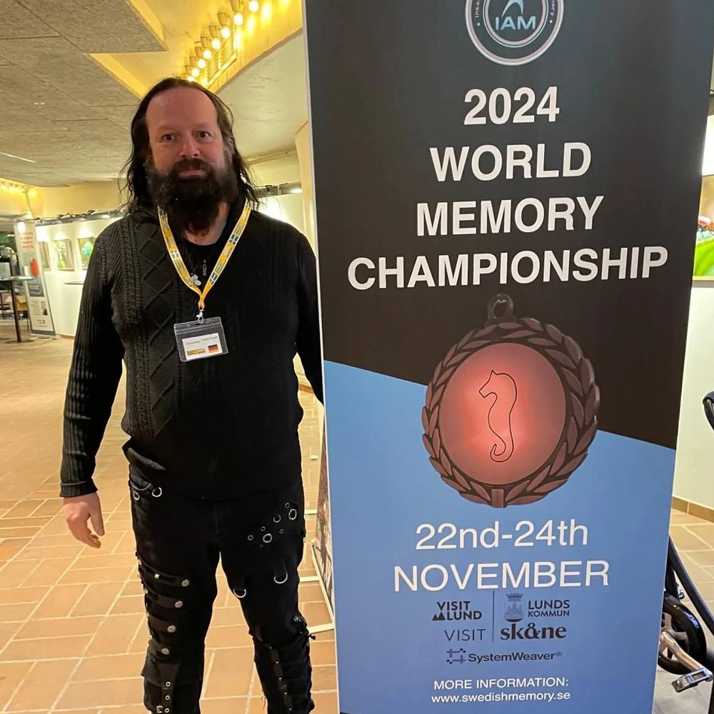 Frank Grube steht neben dem Aufsteller der „2024 World Memory Championship“ in Lund, 22. bis 24. November.